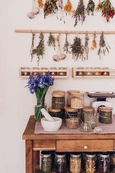 spices and herbs are arranged on a wooden table in front of a wall mounted spice rack