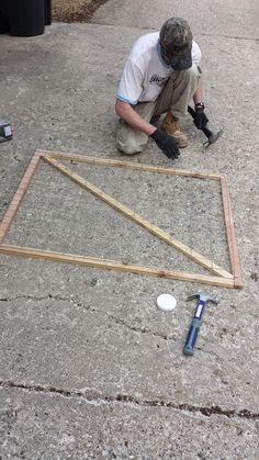 a man kneeling down on the ground working on a piece of wood that has been framed