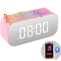 a pink alarm clock with music notes on it and a hand holding a cell phone