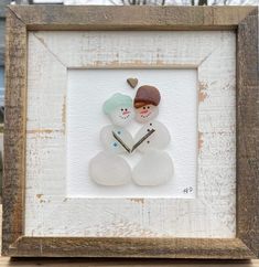 two snowmen in a wooden frame with a heart on the top and one holding a clock