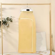 a yellow garment hanging on a clothes rack next to a white vase with flowers in it