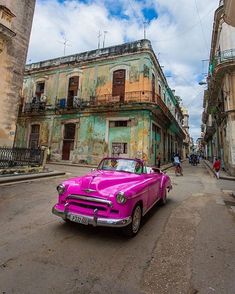 an old pink car parked in front of a building on the side of a street