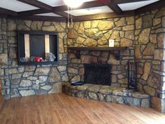 an empty living room with wood floors and stone fireplace