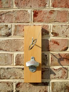 a wooden clock mounted to the side of a brick wall with scissors hanging from it