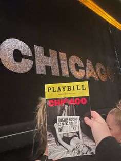 a person is holding up a book in front of a sign that reads chicago playbill chicago