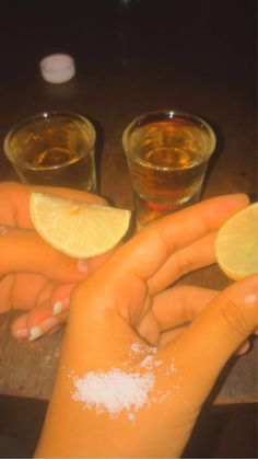 two people holding lemons and salt in their hands on a wooden table with shot glasses