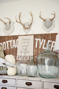 some glass vases are sitting on top of a dresser with antlers above them