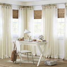 a white desk and chair sitting in front of two windows with drapes on them