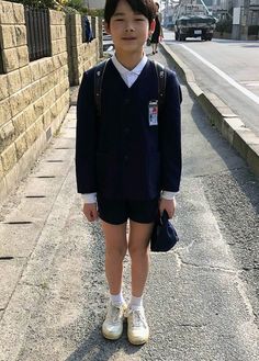 a young boy standing on the side of a road wearing shorts and a school uniform