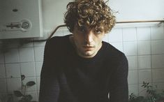 a man with curly hair sitting in a kitchen