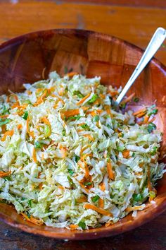 a wooden bowl filled with coleslaw and carrots on top of a table