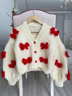 a white cardigan with red flowers on the front and back, sitting on a chair