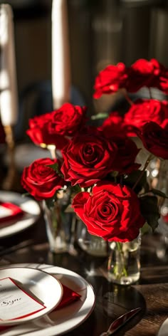 a vase filled with red roses sitting on top of a table next to two plates