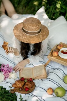 a woman in a straw hat is reading a book and eating fruit on the bed