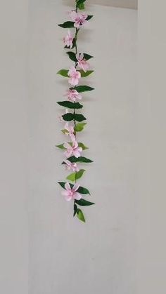 pink flowers and green leaves are hanging from the ceiling in front of a white wall