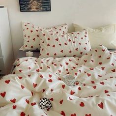 a bed with red hearts on it in a bedroom next to a painting and pillows