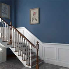 a white stair case next to a blue wall with pictures on the wall above it