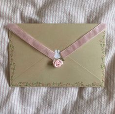 an envelope with a pink ribbon and a flower on it is laying on a bed