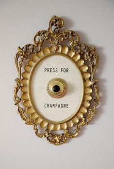 a white clock with the words press for champagne on it's face and an ornate gold frame