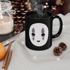 a black coffee mug with an emo face on it next to pine cones and candles