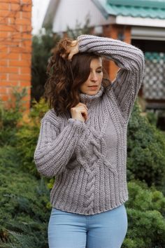 a woman in jeans and a sweater is posing for the camera with her hands on her head