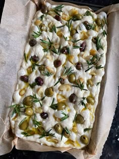 a square pizza with olives, cheese and herbs on it sitting on top of parchment paper