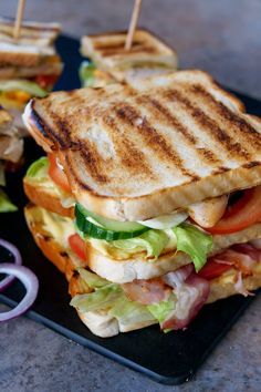 two sandwiches on a black plate with toothpicks in the middle one is cut in half