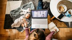 a woman sitting at a table with a laptop computer and doll on her lap top