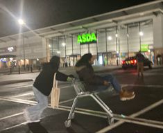 two people pushing a shopping cart in front of a asda store at night time