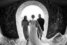 the bride and groom are standing in front of a stone arch with two women looking at them