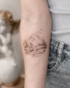 a woman's arm with a tattoo on it that has mountains in the background