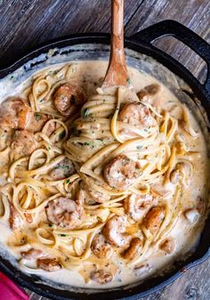 a skillet filled with pasta and meatballs on top of a wooden table next to a pink napkin