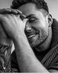 black and white photograph of a man smiling with his hands on his face while wearing a scarf