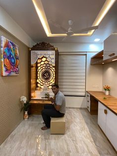 a man sitting on a stool in a room with wooden cabinets and artwork hanging from the ceiling