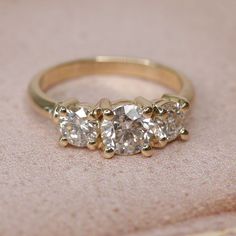 three stone diamond ring sitting on top of a pink cloth covered table with gold trim