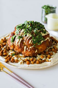 a white plate topped with meat covered in sauce and garnished with green toppings