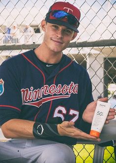 a baseball player sitting in the dugout holding a bottle and sunscreen on his left hand