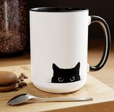 a coffee mug with a black cat's face on the side and spoon next to it