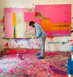 a man standing in front of a painting on the floor with paint all over it