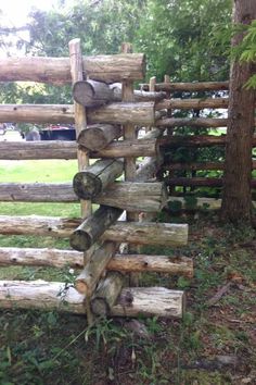 logs stacked on top of each other in front of a wooden fence with grass and trees