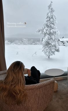 a woman sitting in a chair looking out a window at the snow covered trees outside