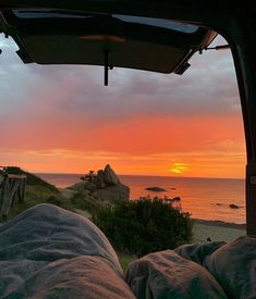 the sun is setting over the ocean from inside a tent with two people sleeping in it