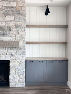 an empty living room with gray cabinets and a stone fireplace in the center, surrounded by white painted walls