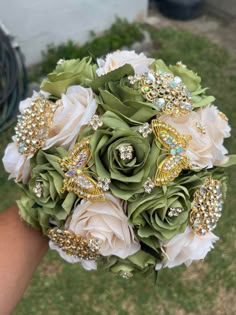 a bridal bouquet with brooches and flowers in the foreground is being held by someone's hand