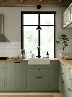 a kitchen with green cabinets and a white sink under a window next to a potted plant