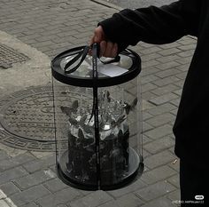 a person is holding a glass container with ice cubes in it on the sidewalk