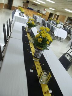 a long table with yellow flowers in vases on it and black runneres down the middle