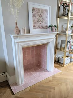 a white fireplace with pink tiles in a living room next to bookshelves and vases