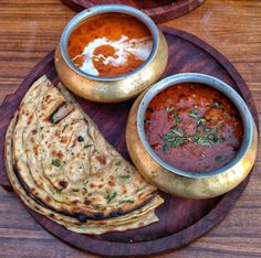 some food is on a wooden plate with sauces and pita bread in bowls