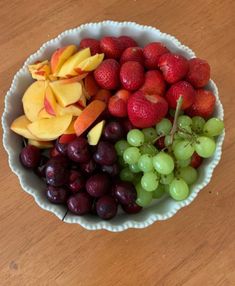 a bowl filled with grapes, strawberries, apples and oranges on top of a wooden table